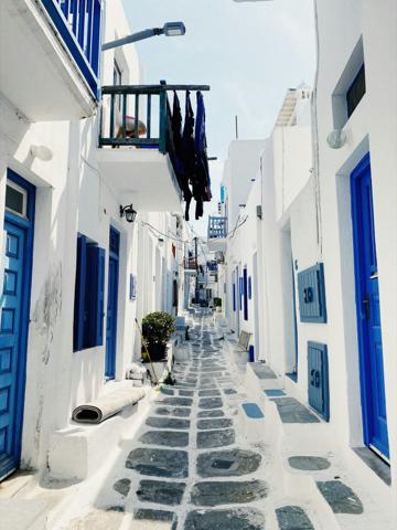 A narrow Mykonian alleyway in Chora — whitewashed walls, blue doors, bougainvillea overhead