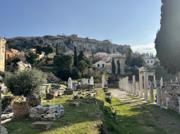 A row of standing columns and scattered marble in an excavated site, the Acropolis on the rock above