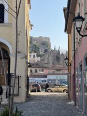 A quiet Athens street of pastel houses ending at the Acropolis rock