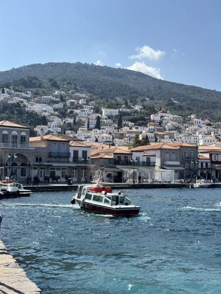 Stone and whitewashed houses stacked around Hydra's harbour, a small boat crossing the water