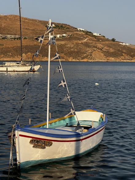 A small wooden fishing boat moored in a calm Cycladic harbour, flag bunting strung from its mast