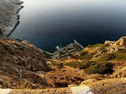 Scrub and pale rock dropping to dark blue sea in late light, Folegandros