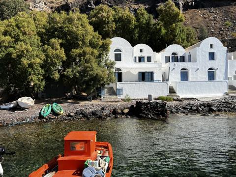 Whitewashed houses and an orange caique in a clear green cove under the volcanic cliff, Santorini