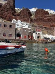 Fishing boats moored in clear water below red volcanic cliffs, Santorini