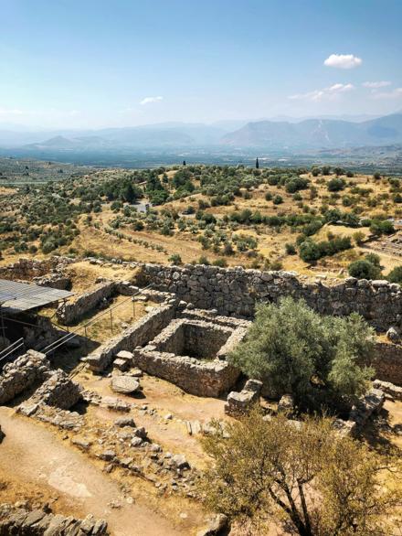 Ruined stone walls at Mycenae among olive trees, with the Argolid hills beyond