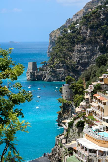 A turquoise cove below Amalfi Coast cliffs, a stone watchtower on the headland and boats at anchor