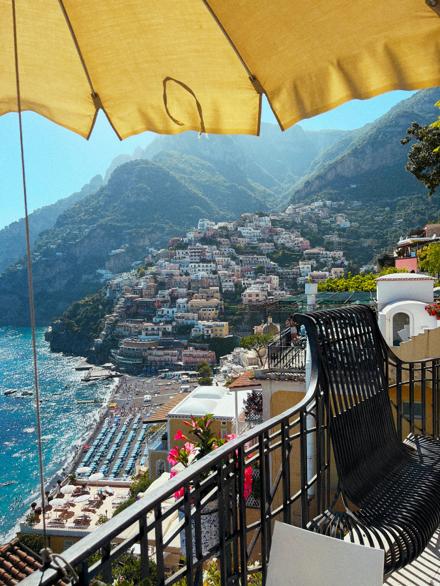 A hotel terrace under a yellow parasol looking down over Positano and the beach below