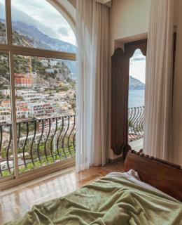 A superior suite bed facing an arched window over the sea