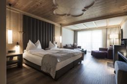 ADLER Spa Resort Dolomiti — guest suite with pine ceiling rosette and dark velvet headboard