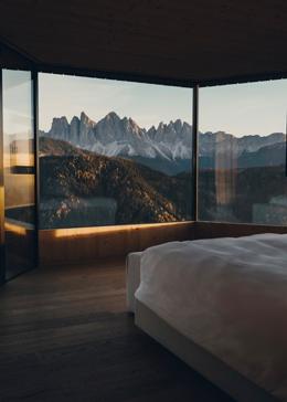 Forestis Dolomites — penthouse bedroom with floor-to-ceiling windows framing the Odle/Geisler range at sunset