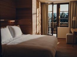 Forestis Dolomites — cozy suite with pale-wood walls and balcony doors framing the mountain at dusk