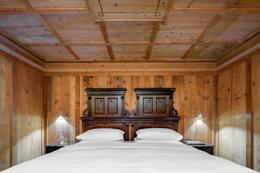Hotel La Perla — Suite Ernesto with carved wood headboard under coffered pine ceiling