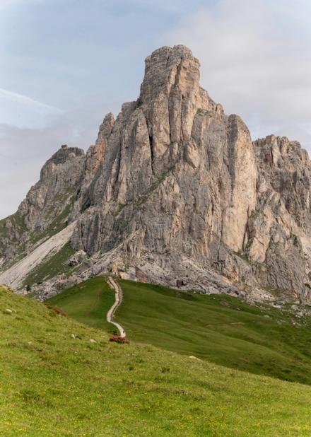 A stepped path climbing a green meadow towards a limestone tower