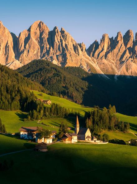 A small church on green meadows below a wall of limestone spires