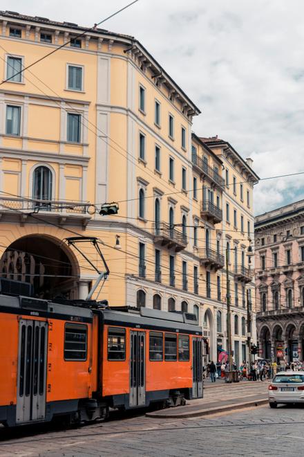 A vintage orange tram passing yellow palazzi in Milan