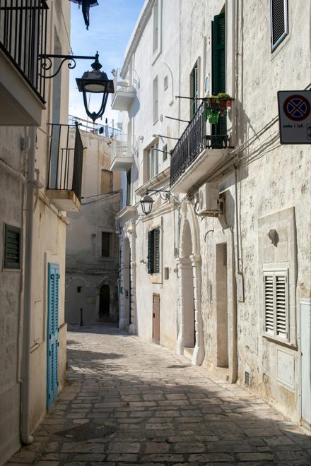 A narrow limestone lane between whitewashed houses, balconies overhead