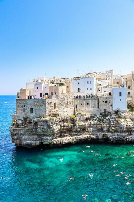 A cliff-top town above a bay of swimmers, houses built to the edge of the rock