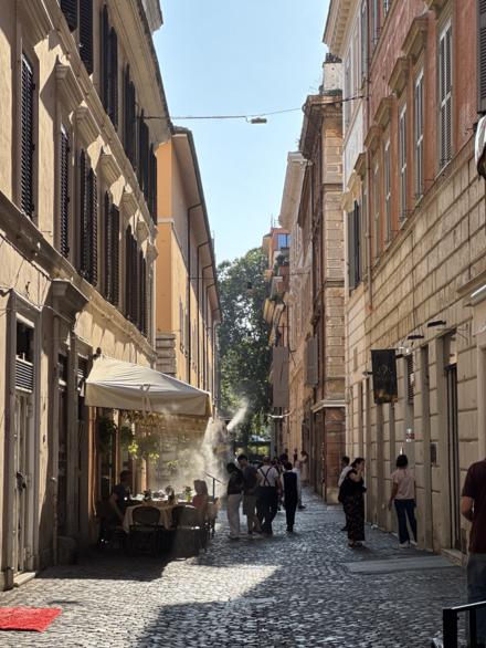A narrow Roman side street with restaurant tables under an awning