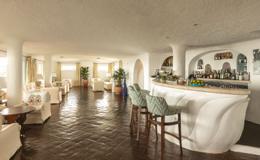 Romazzino — sculptural white plaster bar with green woven stools under a vaulted plaster ceiling