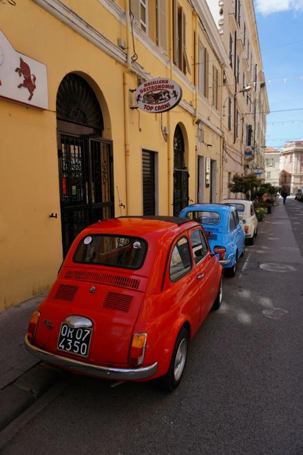 Vintage Fiat 500s parked along a narrow town street