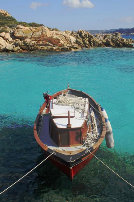 A small wooden boat moored over clear shallows, granite behind it