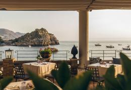 Villa Sant'Andrea — Oliviero restaurant terrace at golden hour, white linen tables, Isola Bella beyond