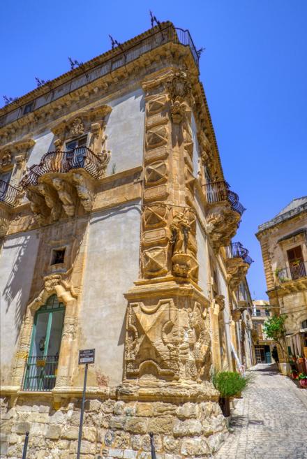 The carved corner of Palazzo Beneventano in Scicli, masks and brackets in honey-coloured stone