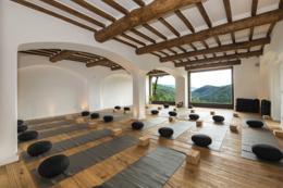 Eremito — sala with exposed wood beams and a panoramic window opening to the forested valley
