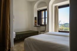 Eremito — a celluzza monk-cell room with whitewashed walls and a forest-view window