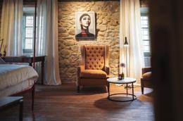 Vocabolo Moscatelli — suite with rough stone walls, ochre velvet wingback, antique writing desk, modernist portrait