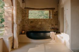 Vocabolo Moscatelli — cantilevered black freestanding bathtub on a stone loggia opening to the forest