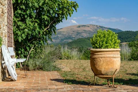 A farmhouse terrace with a terracotta urn, hills behind it