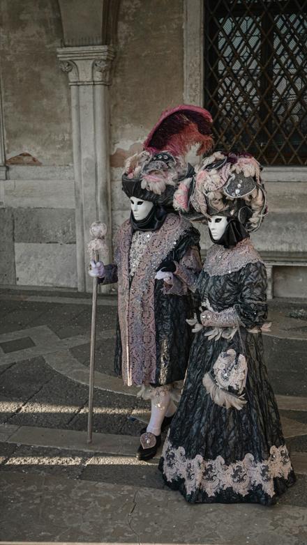 Two figures in full Carnevale costume and white masks under a Gothic arcade