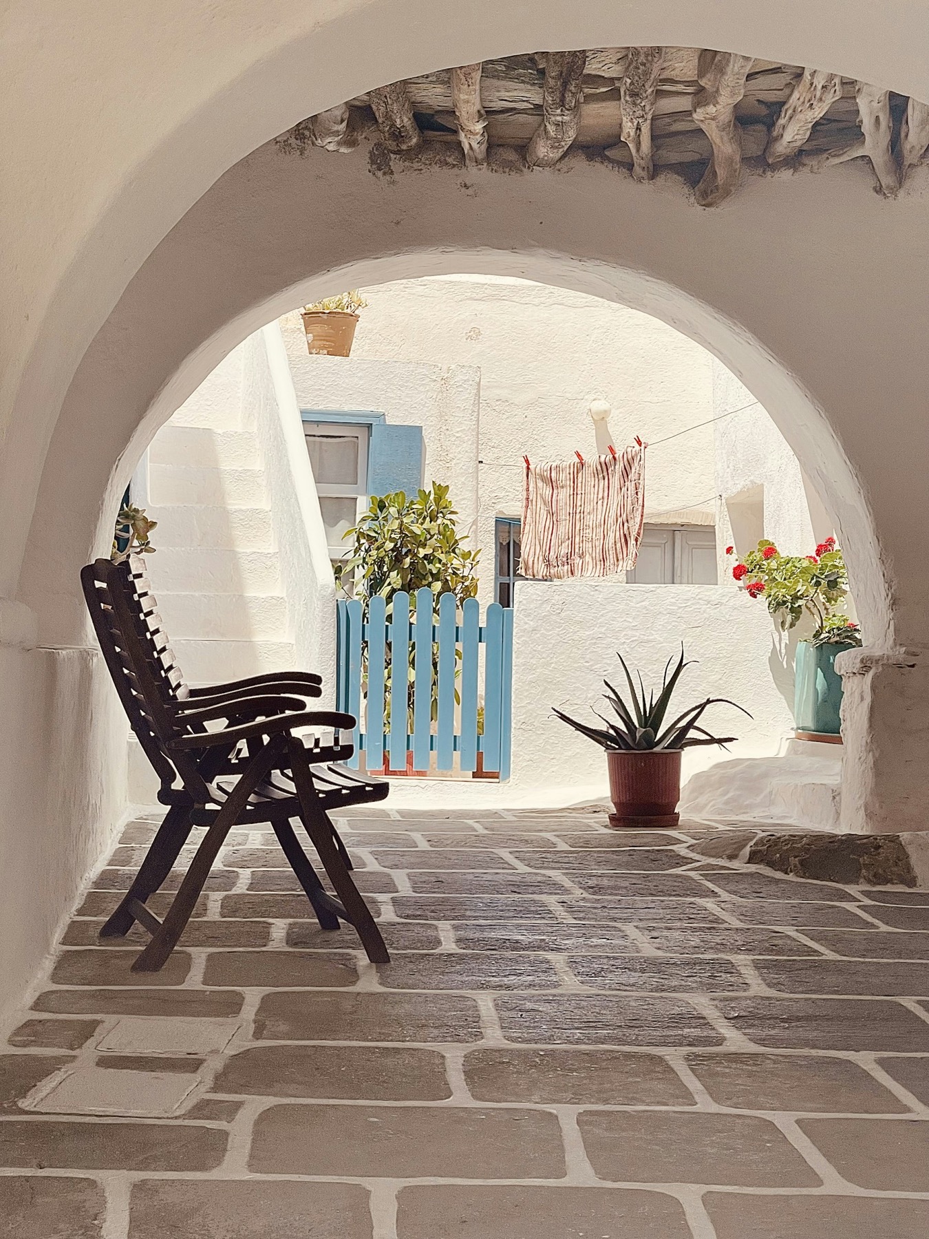 A whitewashed Cycladic arched passageway opening onto a sunlit courtyard with a blue picket gate