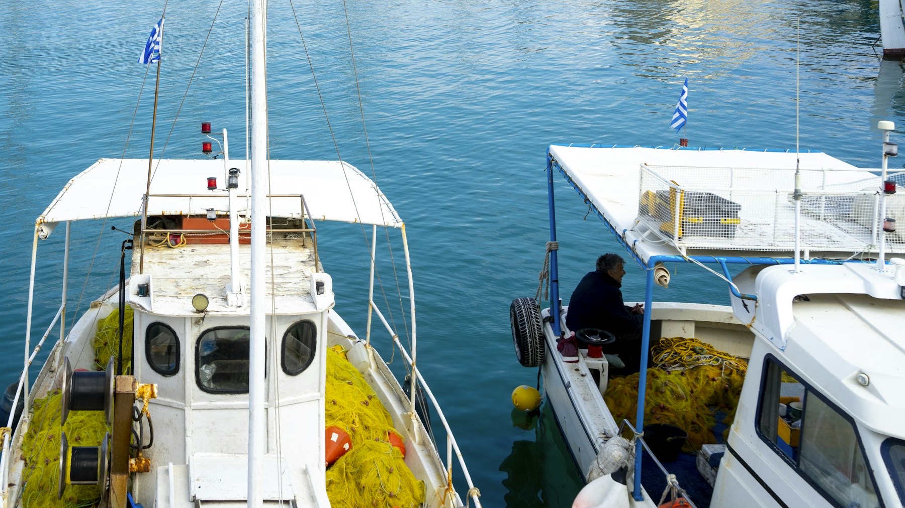 Two Greek fishing boats with national flags moored in a Cycladic harbor