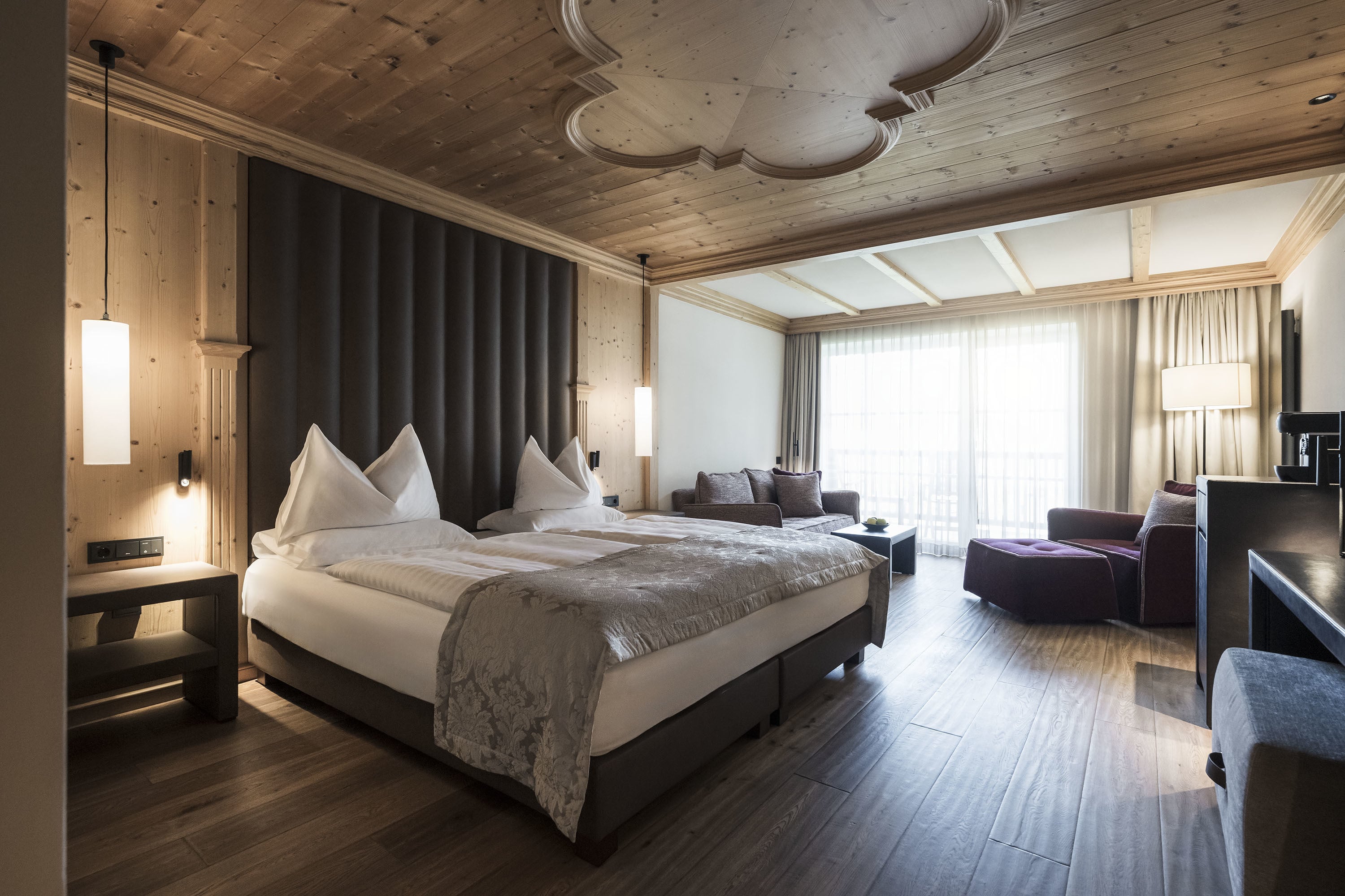 ADLER Spa Resort Dolomiti — guest suite with pine ceiling rosette and dark velvet headboard