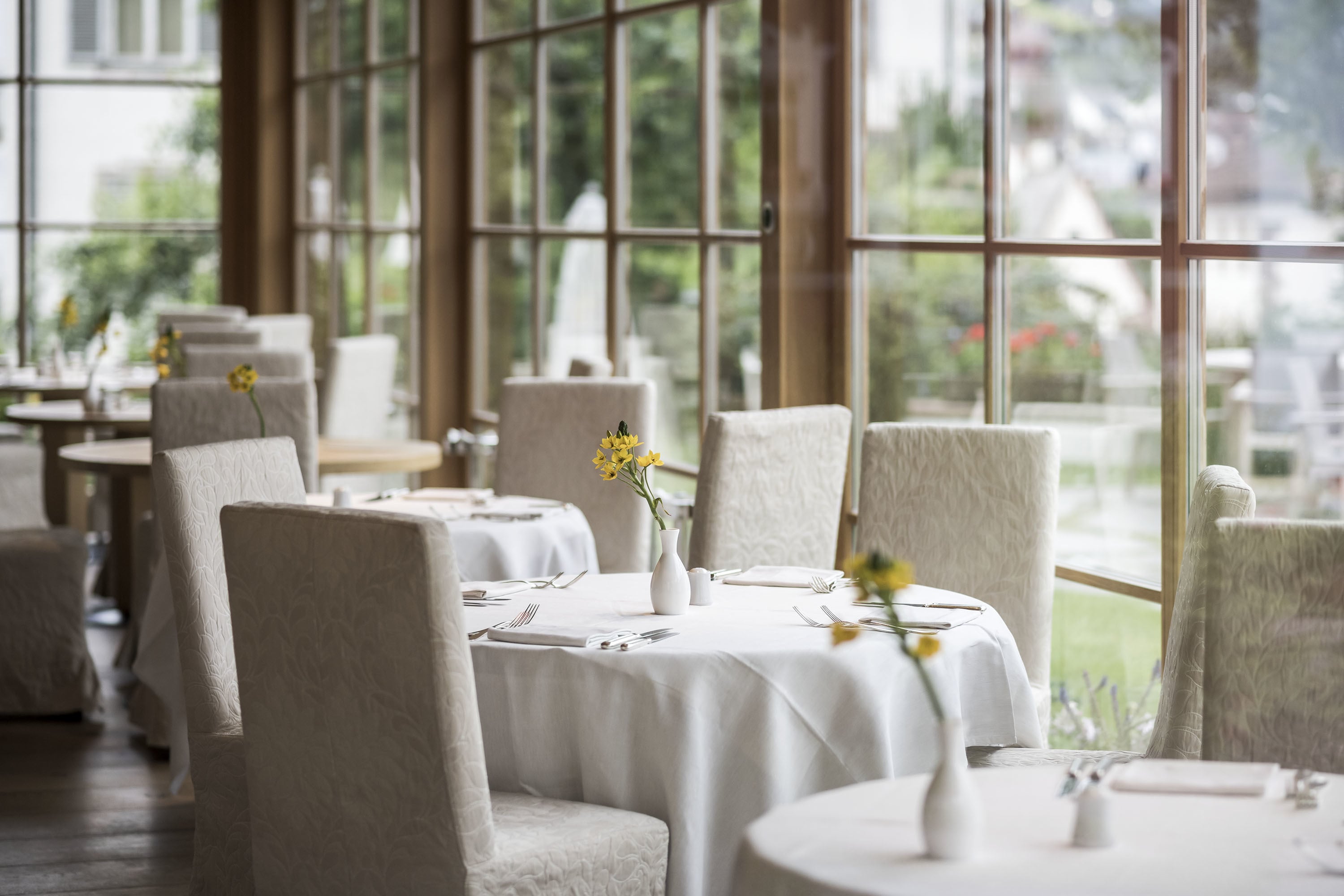 ADLER Spa Resort Dolomiti — dining room with white linens, daffodils, panoramic windows