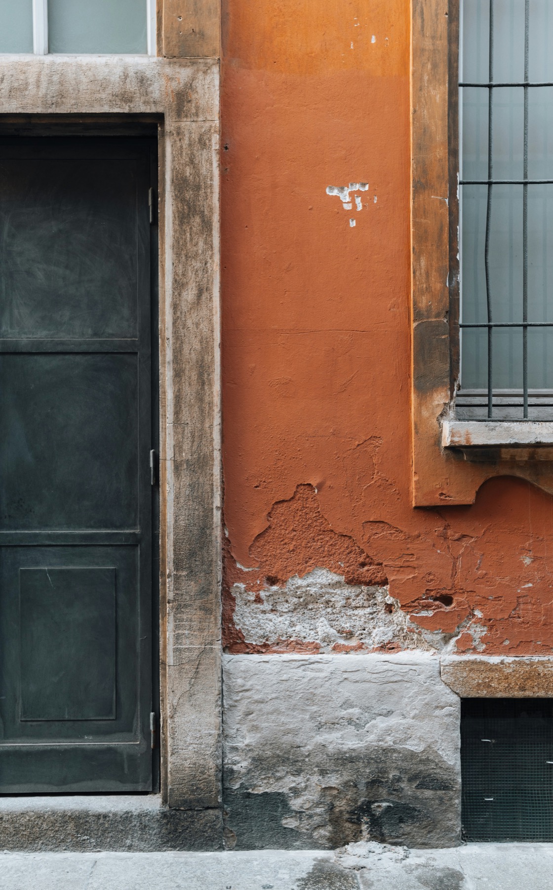 A weathered terracotta-and-grey Milan facade with a green door