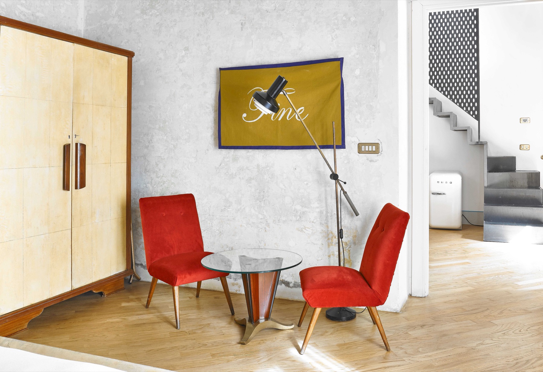 G-Rough — open-plan suite with red mid-century chairs, Fine flag artwork, glass coffee table