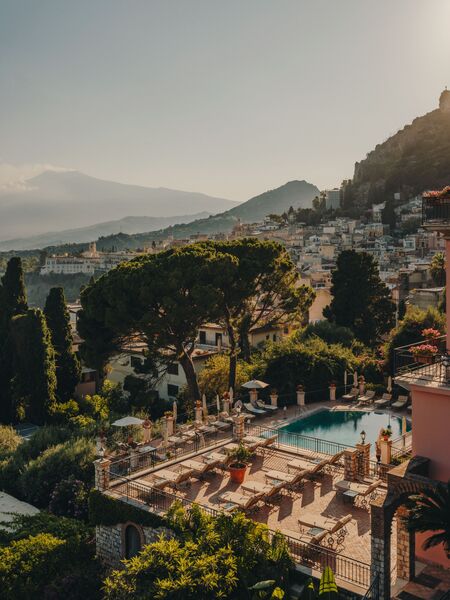 Belmond Grand Hotel Timeo — pool deck at golden hour, Taormina rooftops stretching to Etna on the horizon