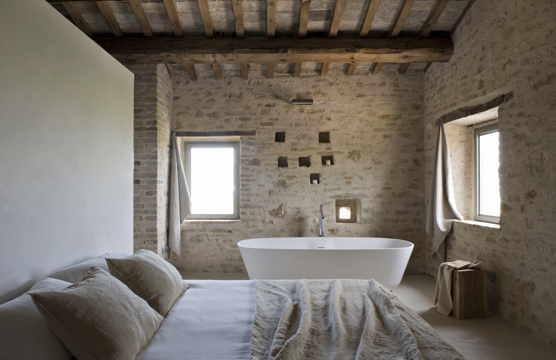 Casa Olivi — bedroom with original stone walls, wood-beamed ceiling, freestanding white bathtub