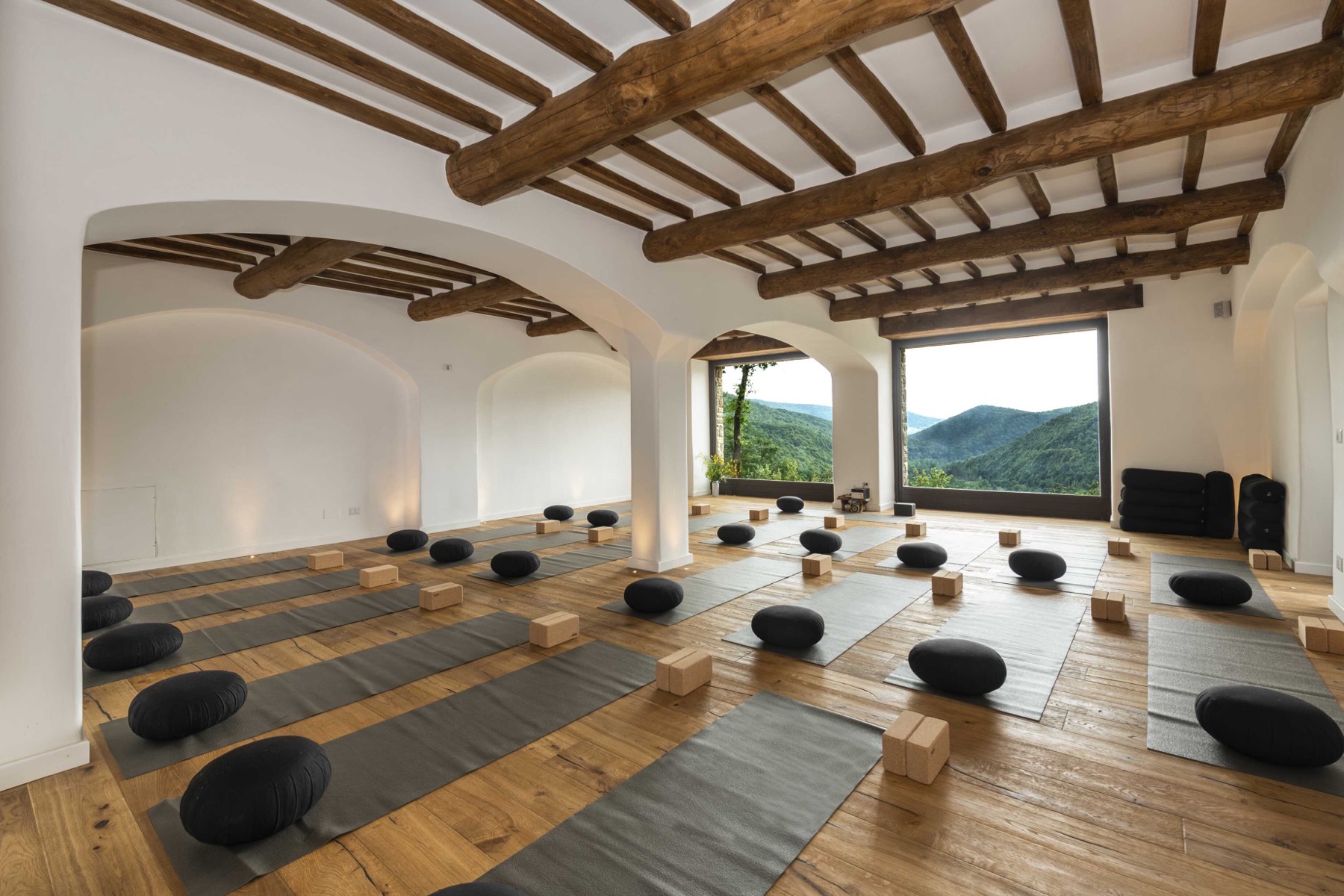 Eremito — yoga sala with exposed wood beams and a panoramic window opening to the forested valley