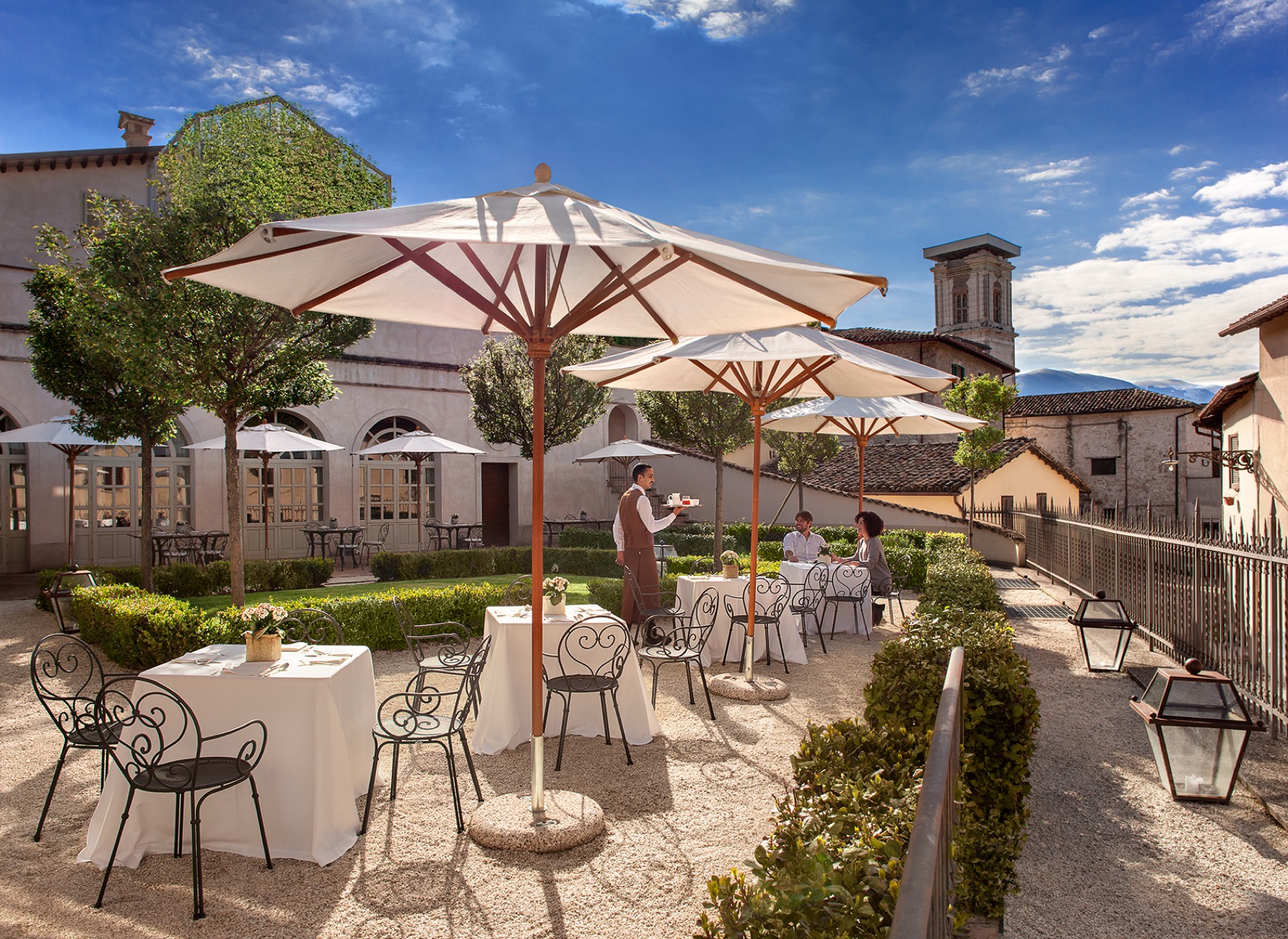 Palazzo Seneca, Norcia — backyard garden with parasols and the historic centre tower